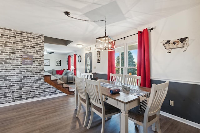 dining room featuring a notable chandelier, brick wall, and dark wood-type flooring