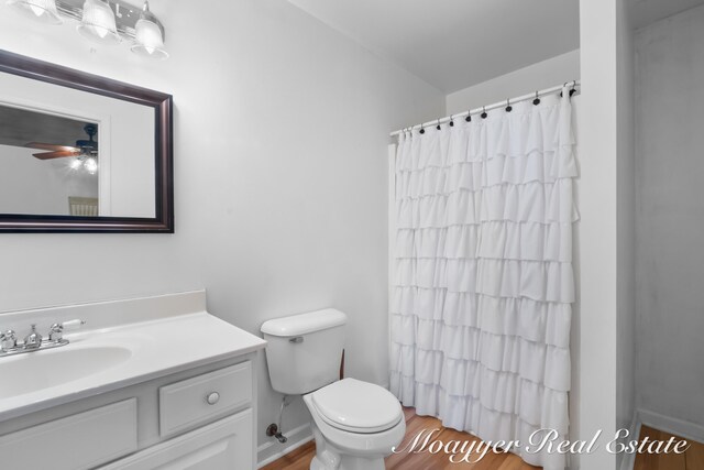 bathroom with hardwood / wood-style floors, ceiling fan, walk in shower, toilet, and vanity