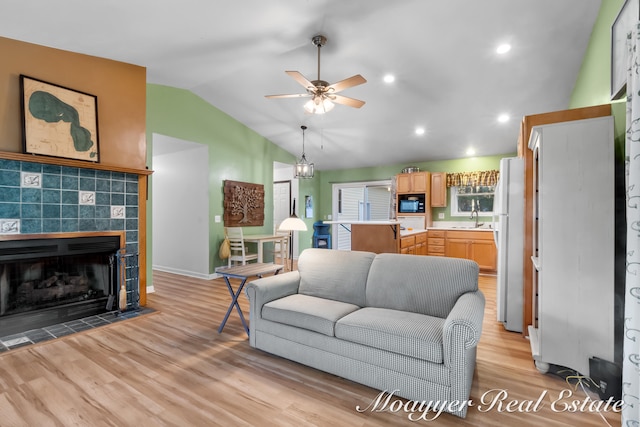 living room with a tiled fireplace, sink, vaulted ceiling, light hardwood / wood-style floors, and ceiling fan