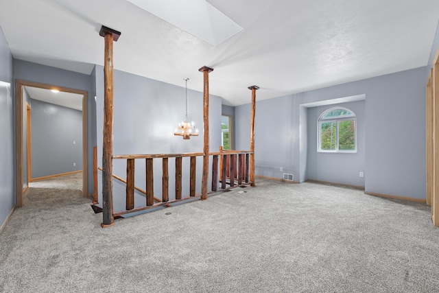 carpeted empty room featuring an inviting chandelier and a skylight