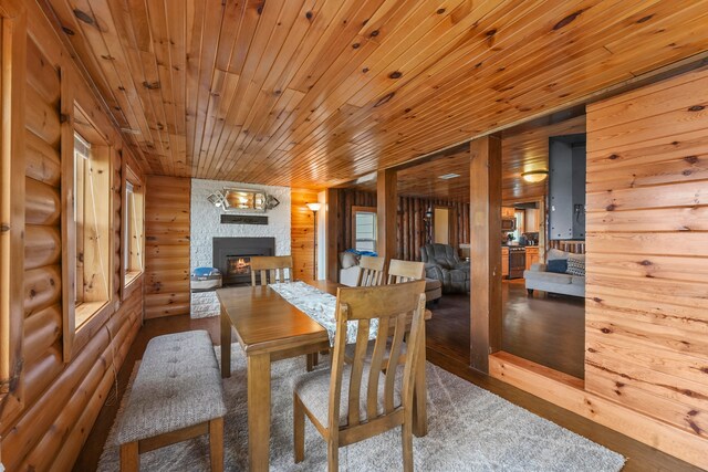 dining area featuring a stone fireplace, hardwood / wood-style floors, and wooden ceiling