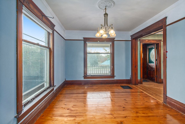 empty room featuring a wealth of natural light, ornamental molding, an inviting chandelier, and light wood-type flooring