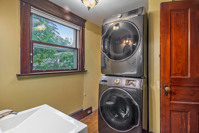 clothes washing area featuring hardwood / wood-style flooring, sink, and stacked washer and clothes dryer