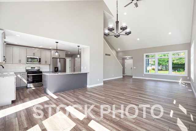 unfurnished living room featuring hardwood / wood-style flooring, high vaulted ceiling, sink, and ceiling fan with notable chandelier