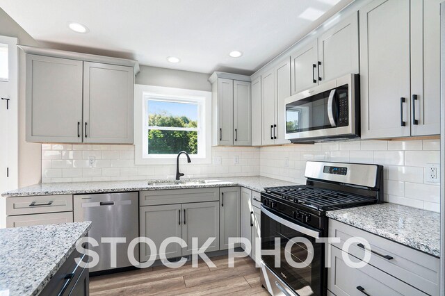 kitchen with tasteful backsplash, light stone counters, appliances with stainless steel finishes, light hardwood / wood-style flooring, and sink