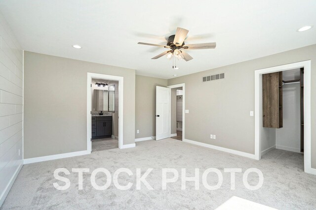 unfurnished bedroom with a closet, light carpet, a walk in closet, ensuite bath, and ceiling fan