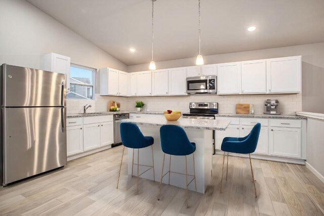 kitchen with appliances with stainless steel finishes, a center island, light stone counters, white cabinets, and vaulted ceiling