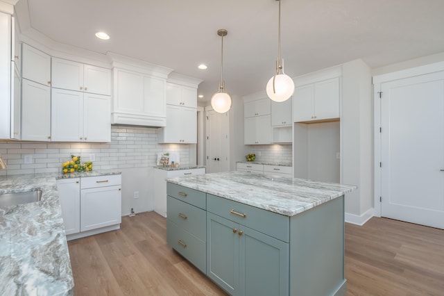 kitchen featuring white cabinets, hanging light fixtures, backsplash, light wood-type flooring, and a center island