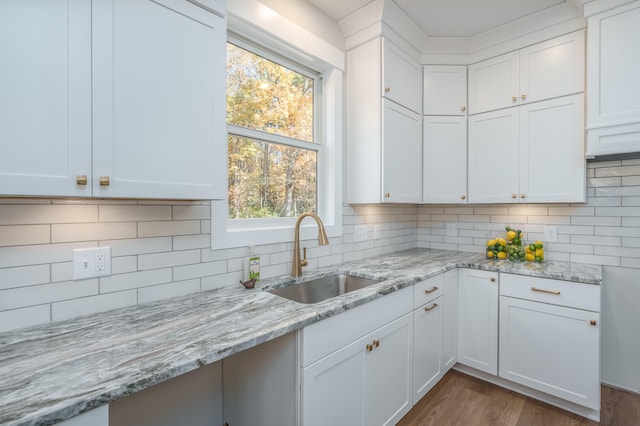 kitchen with light stone counters, hardwood / wood-style flooring, sink, and white cabinets