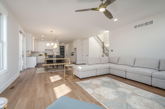 living room with light hardwood / wood-style flooring and ceiling fan with notable chandelier