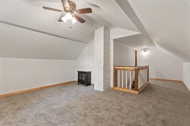 bonus room featuring a wood stove, carpet floors, a textured ceiling, and vaulted ceiling