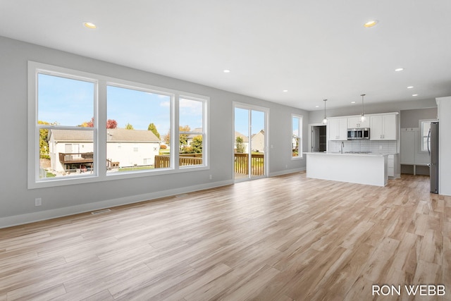 unfurnished living room with sink, a wealth of natural light, and light wood-type flooring