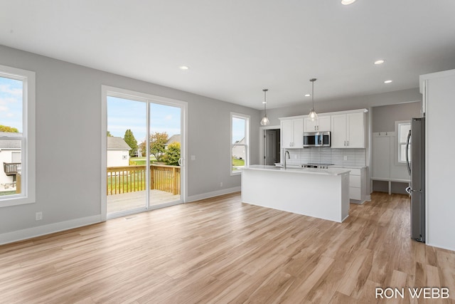 kitchen with appliances with stainless steel finishes, white cabinets, hanging light fixtures, and plenty of natural light