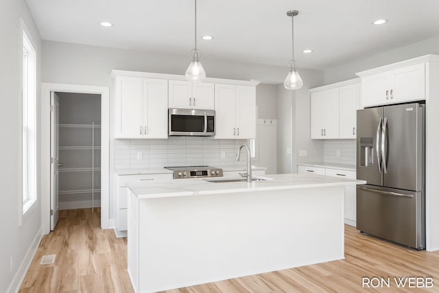 kitchen with sink, stainless steel appliances, pendant lighting, white cabinets, and a kitchen island with sink