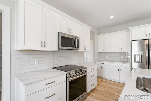 kitchen with decorative backsplash, appliances with stainless steel finishes, white cabinetry, light stone countertops, and light wood-type flooring