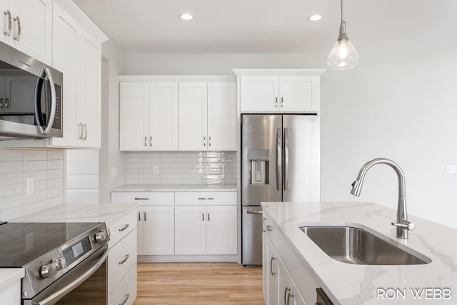 kitchen with hanging light fixtures, appliances with stainless steel finishes, white cabinetry, light stone countertops, and sink