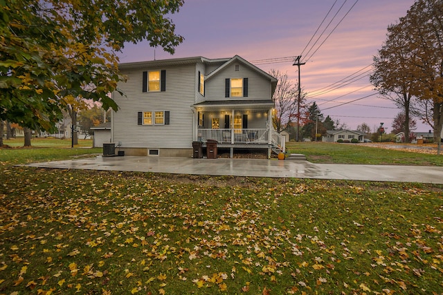 back house at dusk featuring covered porch, a lawn, and cooling unit