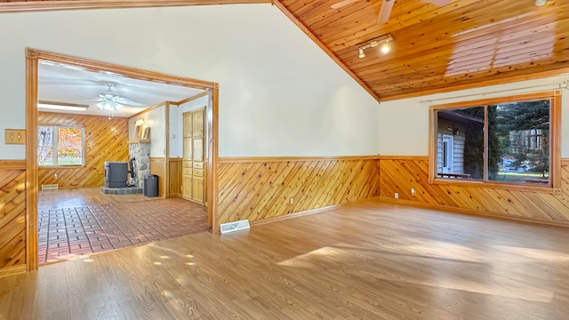 spare room featuring a wood stove, hardwood / wood-style flooring, wooden ceiling, and ceiling fan