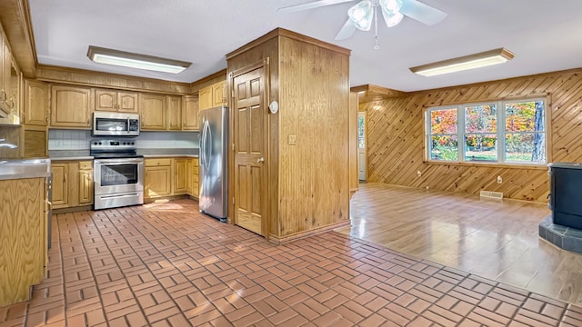 kitchen featuring wooden walls, appliances with stainless steel finishes, ceiling fan, and tasteful backsplash