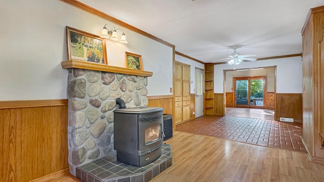 living room with ceiling fan, a textured ceiling, hardwood / wood-style flooring, crown molding, and a wood stove