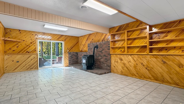 unfurnished living room with light tile patterned flooring, built in shelves, a wood stove, and wood walls