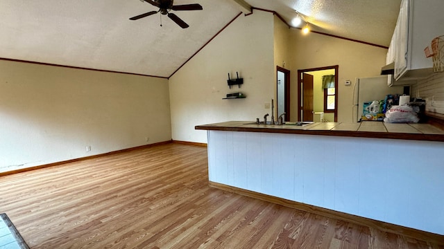 kitchen featuring white cabinetry, a textured ceiling, light wood-type flooring, vaulted ceiling with beams, and tile counters