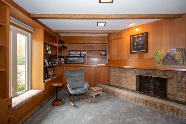 living area featuring beamed ceiling, wooden walls, a fireplace, and carpet