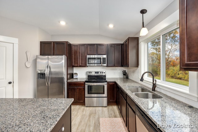 kitchen with vaulted ceiling, hanging light fixtures, sink, light stone countertops, and appliances with stainless steel finishes