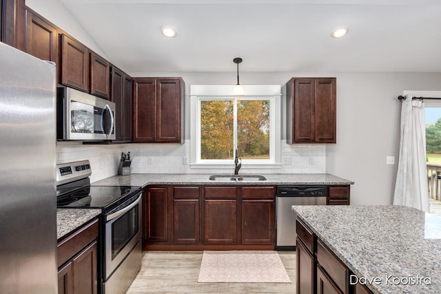 kitchen with tasteful backsplash, light stone counters, stainless steel appliances, pendant lighting, and sink