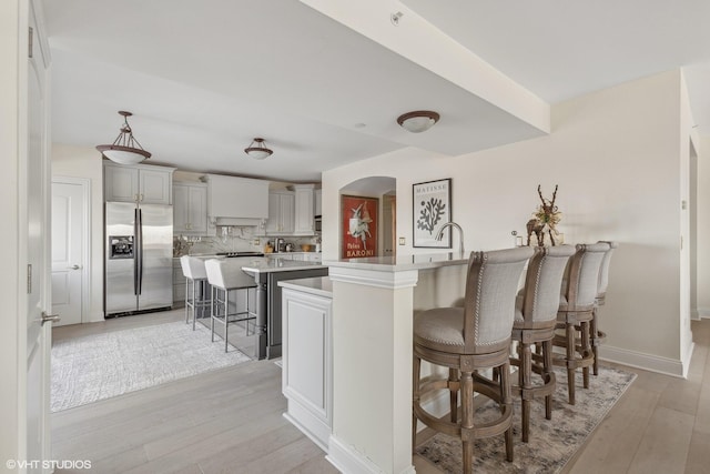 kitchen with tasteful backsplash, stainless steel fridge, light hardwood / wood-style floors, a breakfast bar area, and a kitchen island with sink