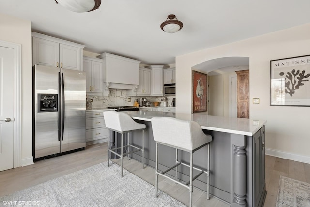 kitchen featuring a breakfast bar, light hardwood / wood-style floors, appliances with stainless steel finishes, and tasteful backsplash