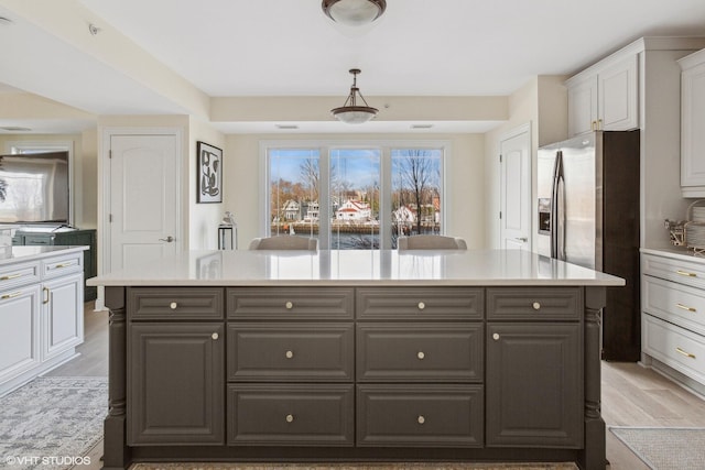 kitchen featuring white cabinetry, a center island, stainless steel fridge, light hardwood / wood-style floors, and decorative light fixtures