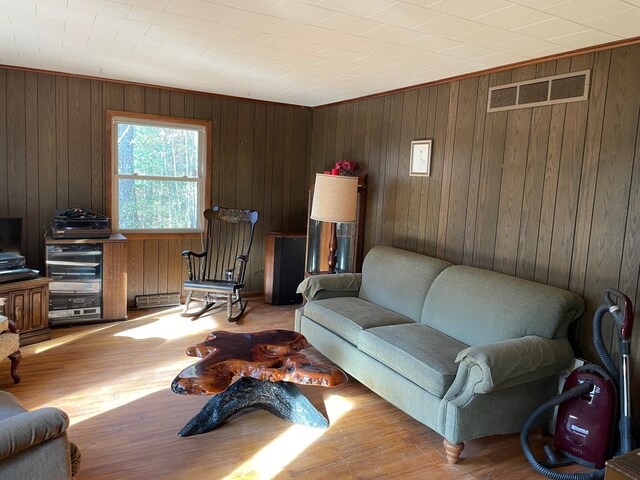 living room with light hardwood / wood-style flooring, wood walls, a baseboard radiator, and crown molding