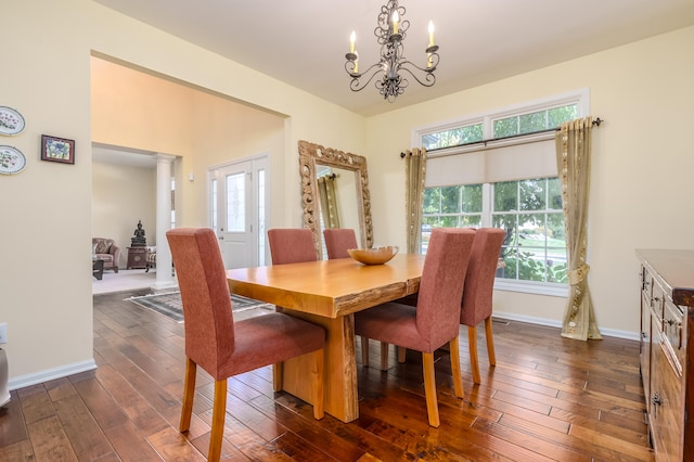 dining space with dark hardwood / wood-style floors, ornate columns, and an inviting chandelier