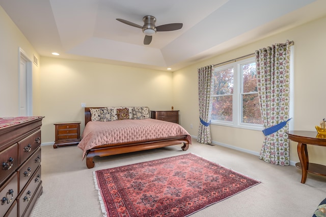 bedroom with ceiling fan, light carpet, and a tray ceiling