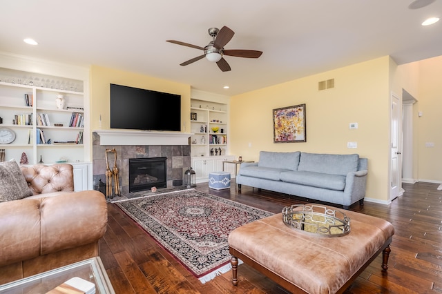 living room featuring ceiling fan, built in features, dark wood-type flooring, and a tile fireplace