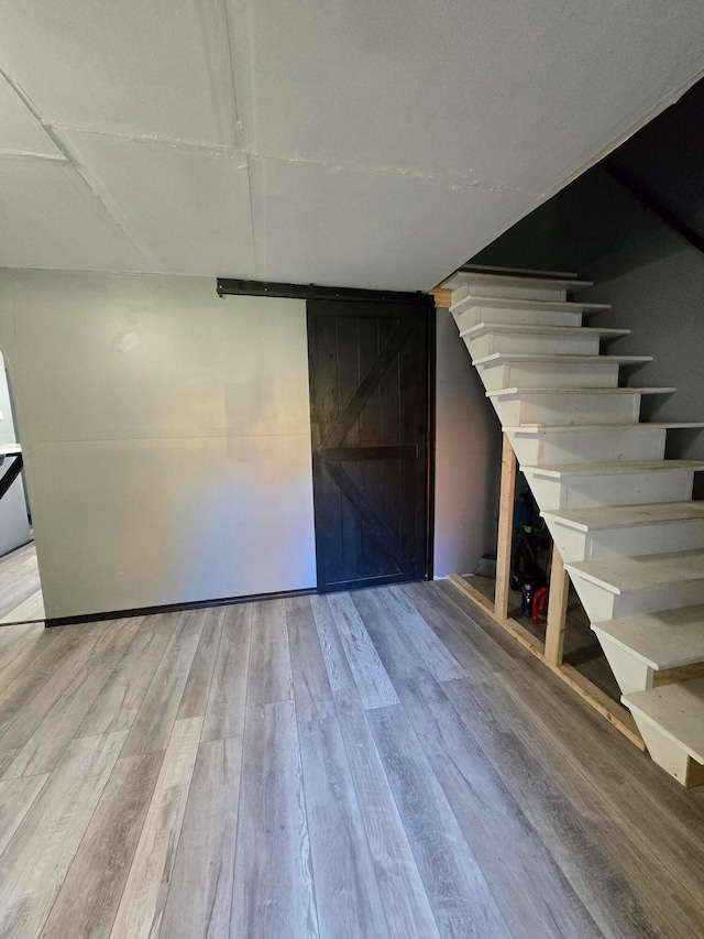 basement with wooden walls, light wood-type flooring, and a barn door