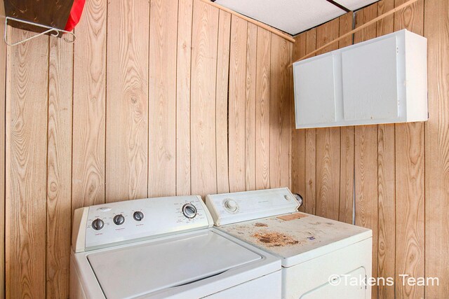 washroom featuring independent washer and dryer, a textured ceiling, cabinets, and wooden walls