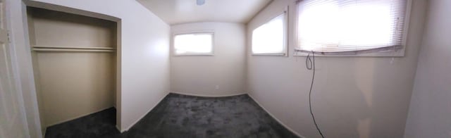 unfurnished bedroom featuring multiple windows, dark carpet, and a closet