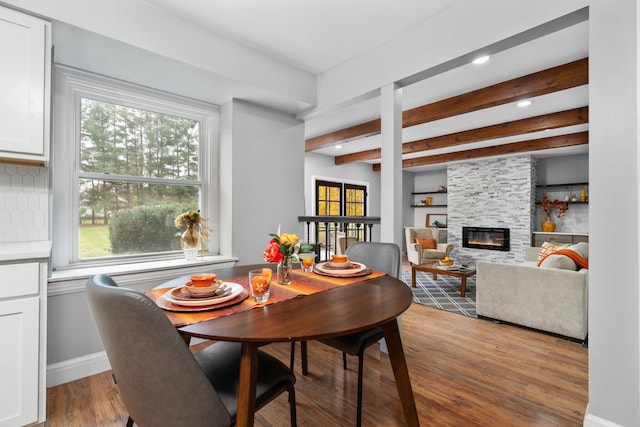 dining space with beam ceiling, hardwood / wood-style flooring, and a fireplace