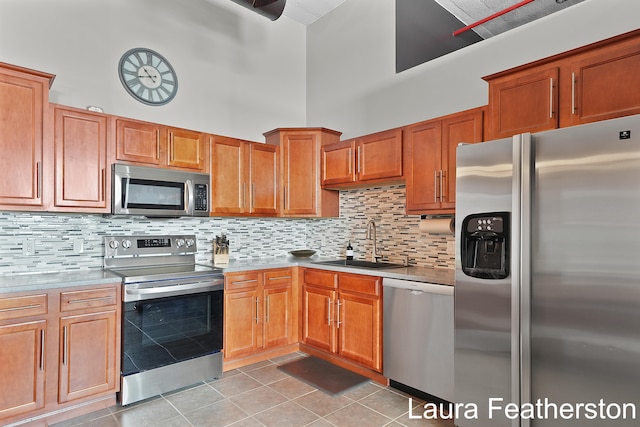 kitchen featuring tasteful backsplash, a towering ceiling, sink, stainless steel appliances, and light tile patterned floors