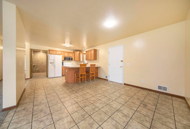 kitchen with a kitchen island, light tile patterned floors, white refrigerator with ice dispenser, and a breakfast bar area