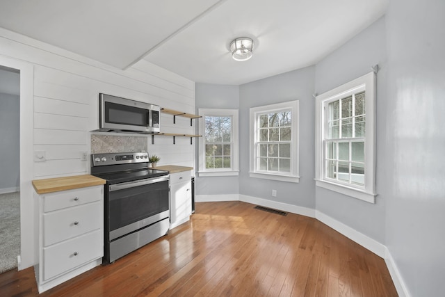 kitchen with decorative backsplash, stainless steel appliances, white cabinets, butcher block countertops, and light hardwood / wood-style floors