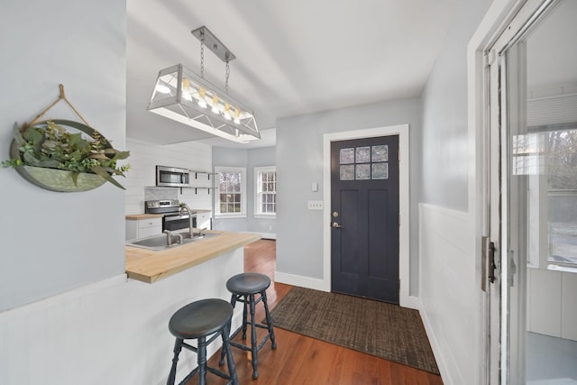 interior space featuring appliances with stainless steel finishes, a kitchen bar, butcher block counters, hanging light fixtures, and dark wood-type flooring