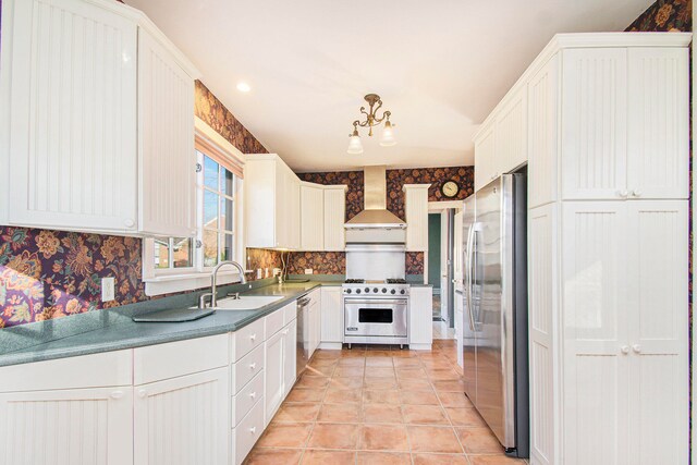 kitchen with appliances with stainless steel finishes, white cabinets, wall chimney range hood, and sink