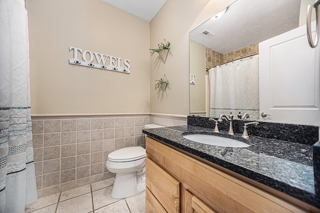 bathroom featuring a textured ceiling, toilet, tile patterned floors, tile walls, and vanity