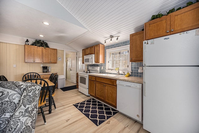 kitchen with lofted ceiling, sink, light hardwood / wood-style floors, wooden walls, and white appliances