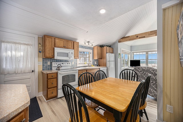 dining area with sink, light wood-type flooring, vaulted ceiling, and a wealth of natural light