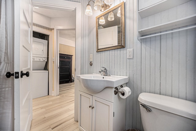 bathroom featuring wood-type flooring, toilet, wooden walls, vanity, and stacked washer / dryer