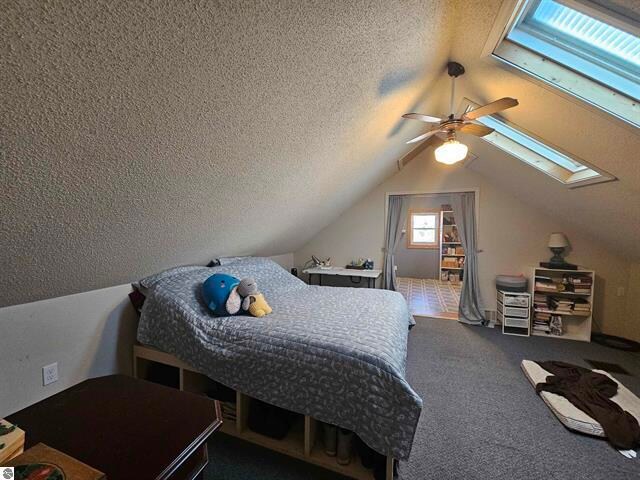 carpeted bedroom featuring lofted ceiling with skylight, a textured ceiling, and ceiling fan